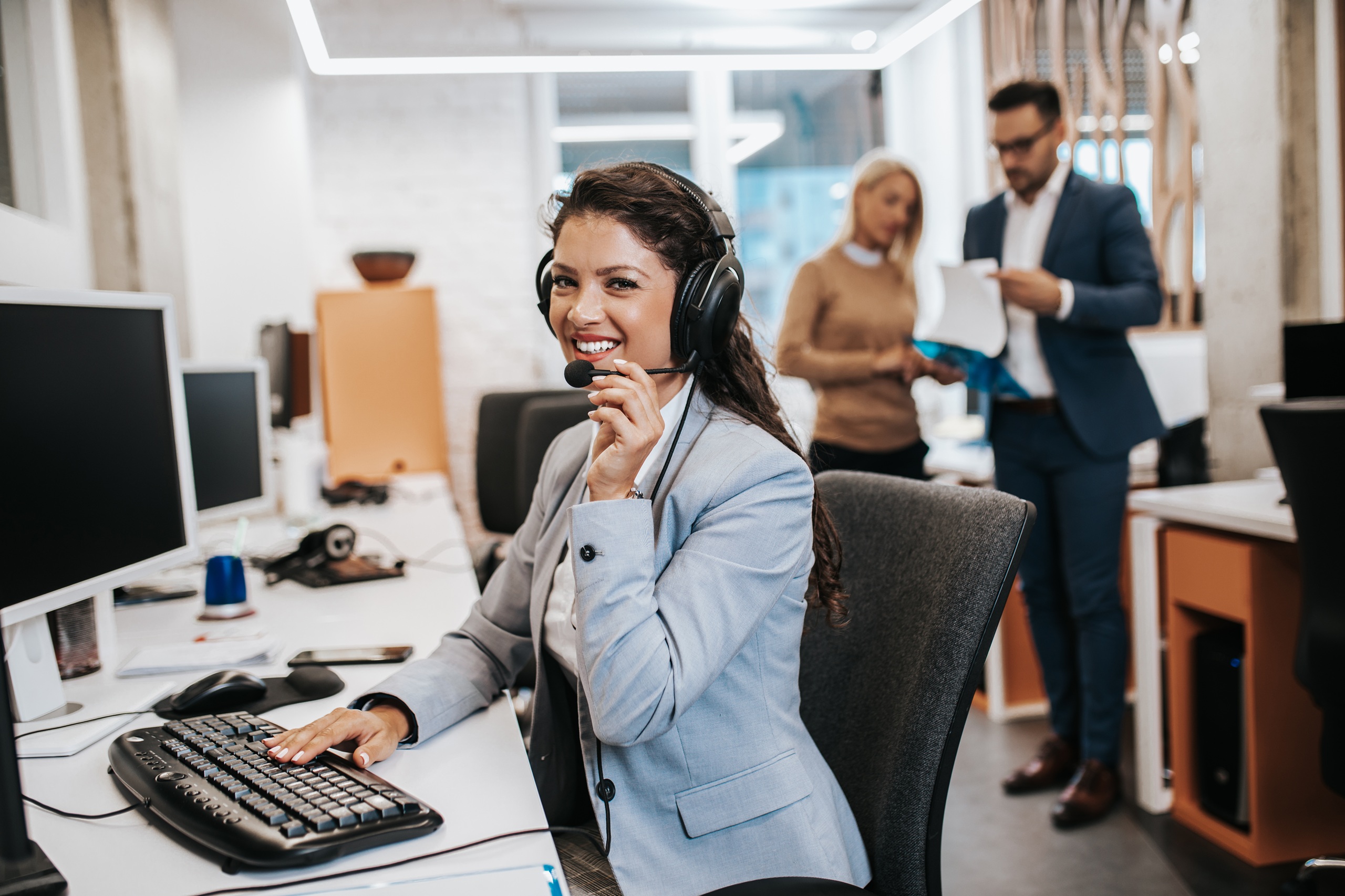 Portrait of beautiful smiling female call-center agent with headset working on support in the office.