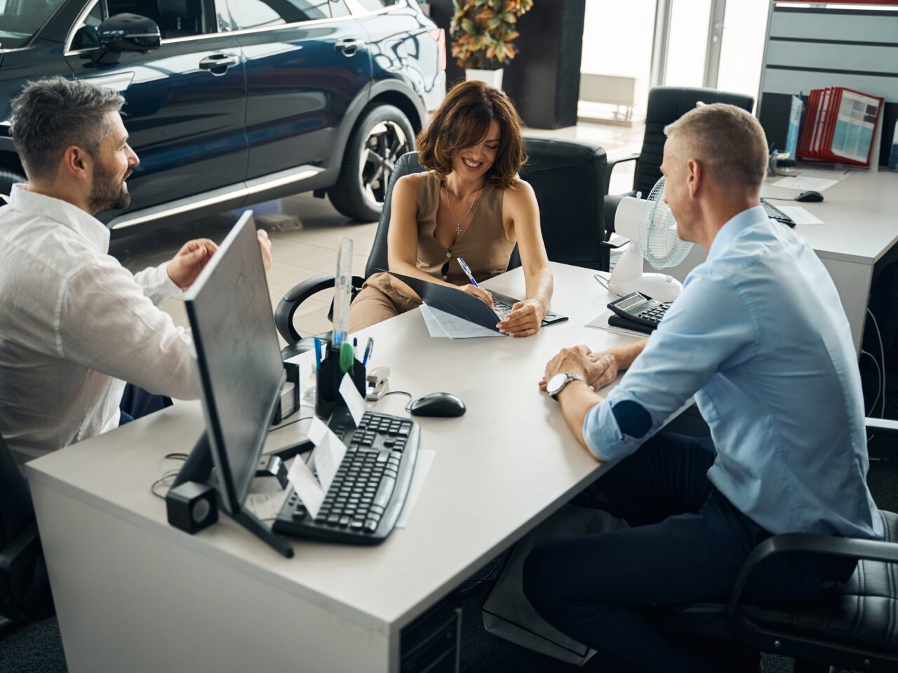 Couple buying new car, lady signing documents in modern auto showroom. Car selling, business concept